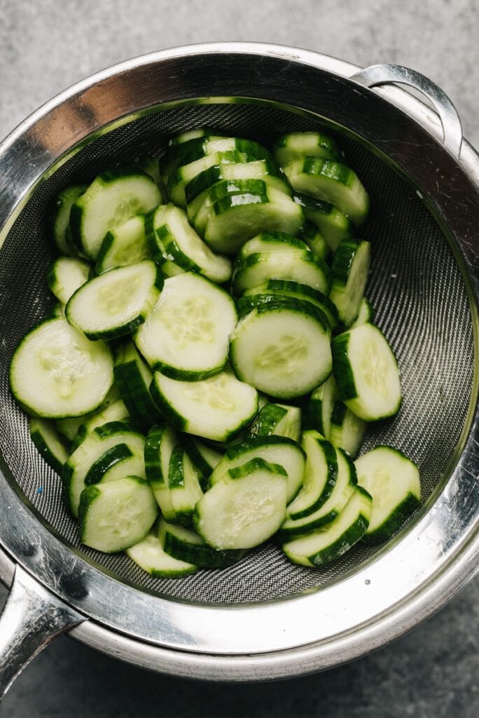 Salted cucumbers draining in a mesh strainer.