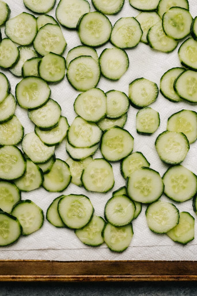 Salted cucumbers draining on a paper towel lined baking sheet.