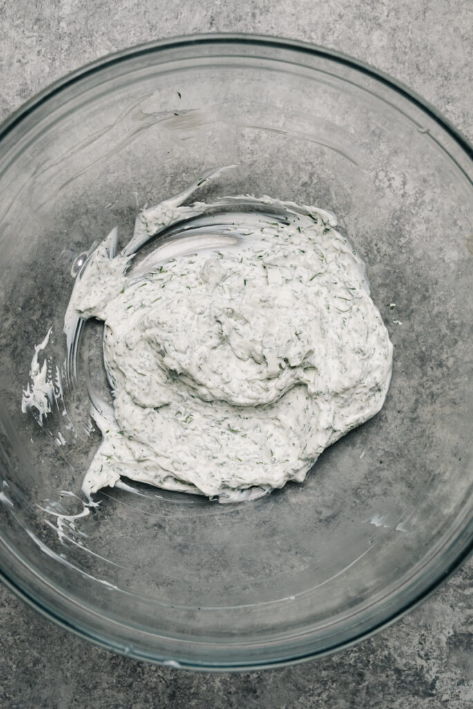 Creamy sour cream dressing with dill and greek yogurt in a glass mixing bowl.