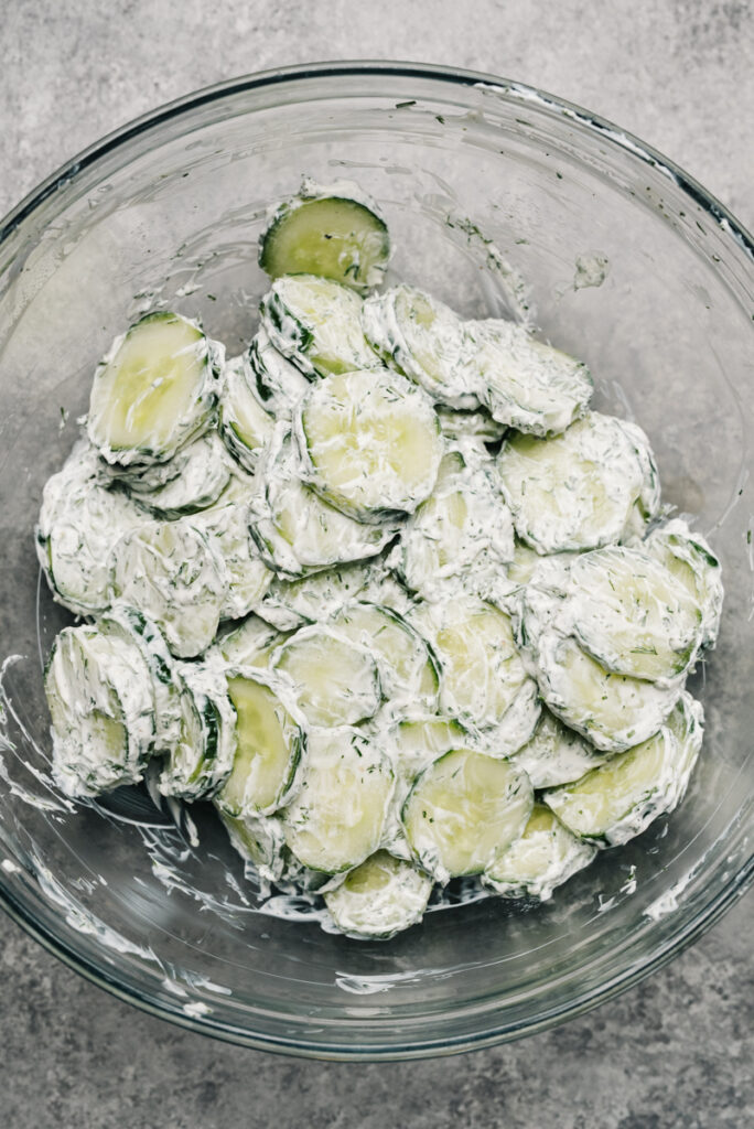 Cucumbers tossed with creamy dill dressing in a glass mixingn bowl.