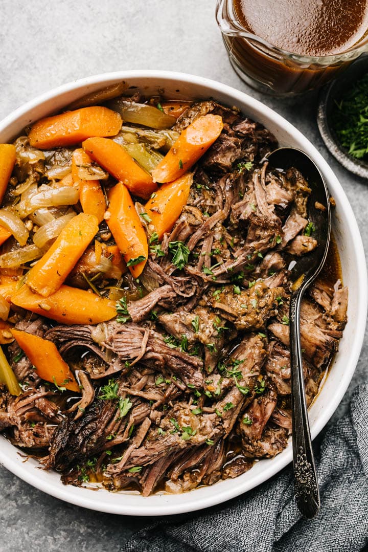 Slow cooker pot roast with carrots and celery in a white serving bowl, garnished with fresh chopped thyme.