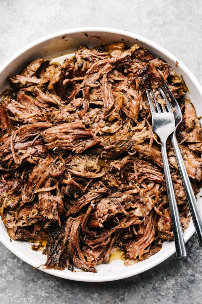 Shredded pot roast in a white bowl with two forks.