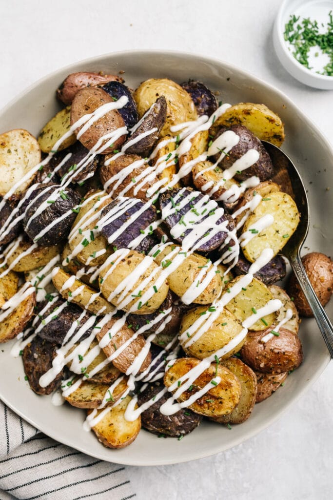 Roasted ranch potatoes in a serving bowl, topped with ranch dressing and minced chives.