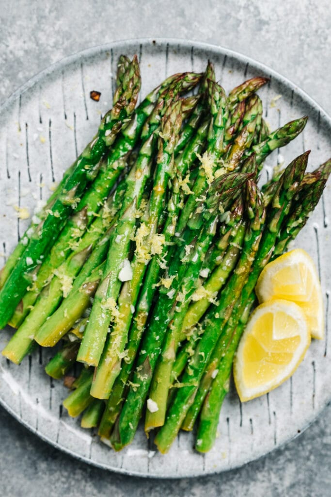 Roasted asparagus with garlic and fresh lemon on a gray plate.