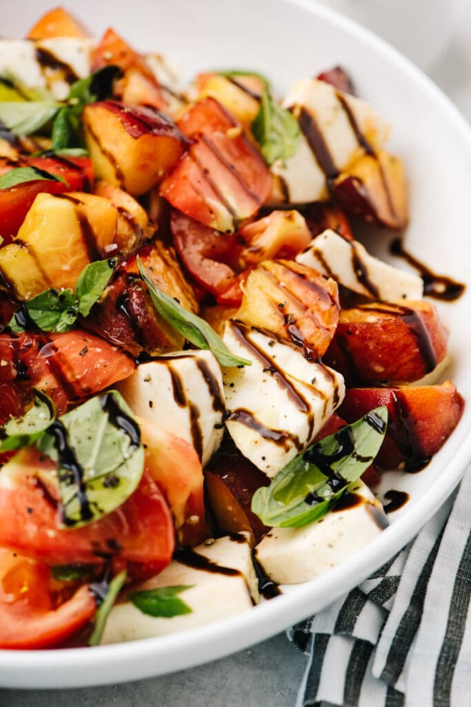 Side view, a caprese salad with fresh peaches in a white serving bowl.