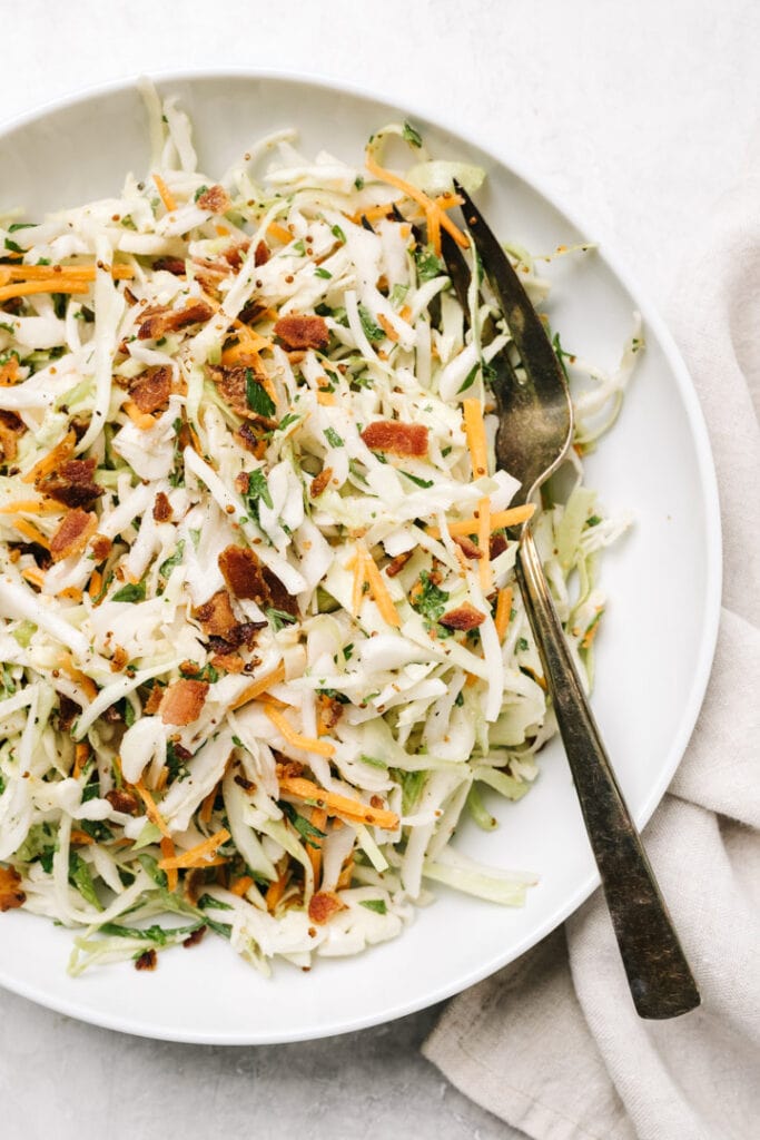 Low carb bacon coleslaw in a white serving bowl with a silver serving fork.