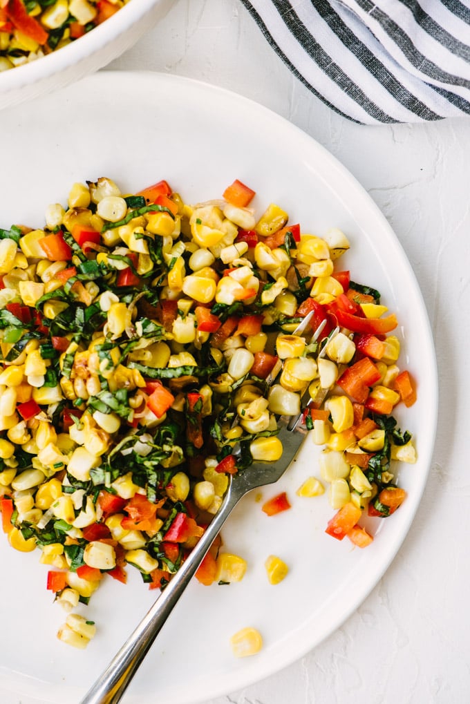 A summer roasted corn salad on a white plate with bell peppers and basil.