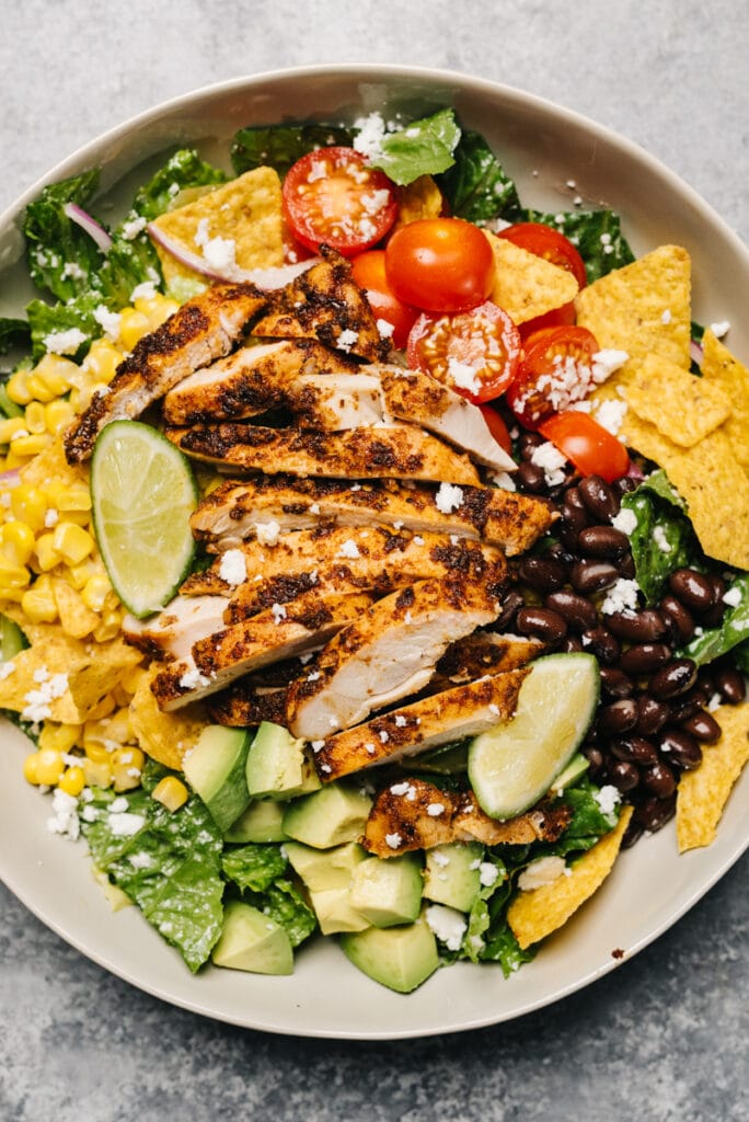 Chicken taco salad in a low tan bowl, with corn, black beans, avocado, and tomato.