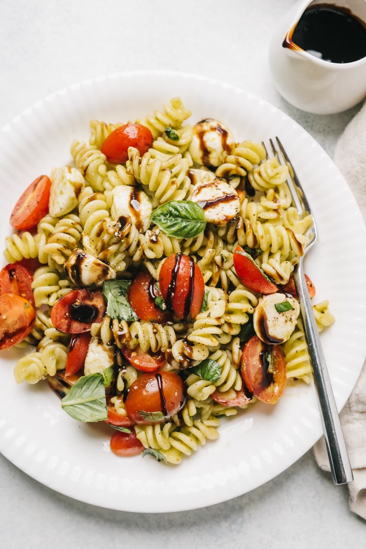 Caprese pasta salad in a white bowl with dressing on the side.