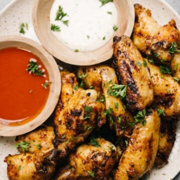 A plate of grilled chicken wings with 2 dipping sauces in small bowls on the side.