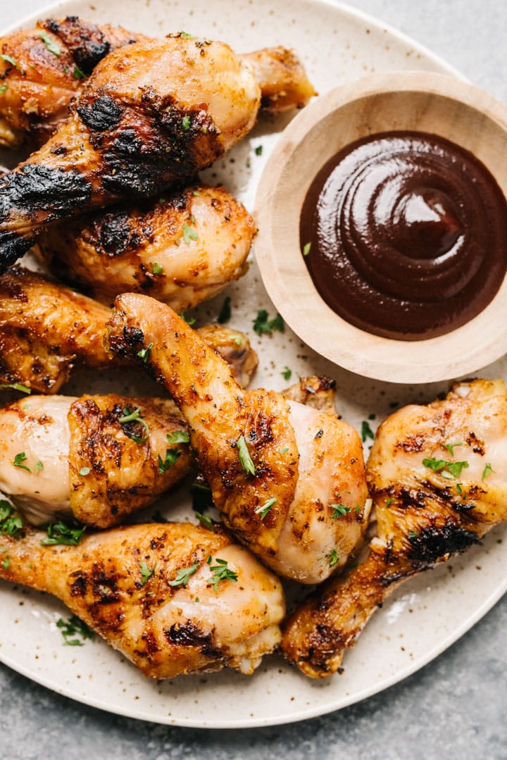A plate filled with grilled chicken drumsticks and a side of BBQ dipping sauce. 