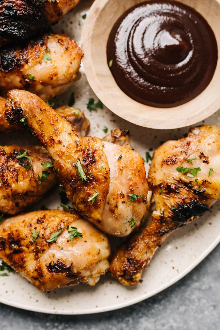 Grilled chicken legs on a plate with a dipping sauce. 