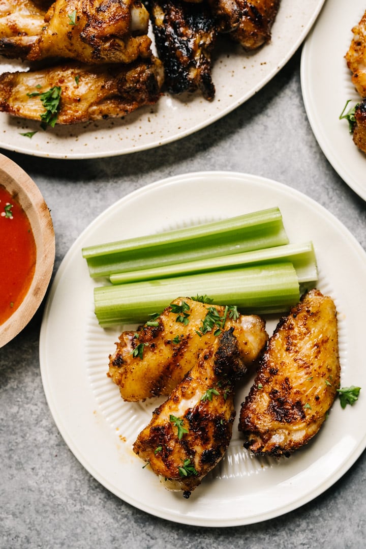 Grilled chicken wings on a plate with celery and dipping sauce on the side. 