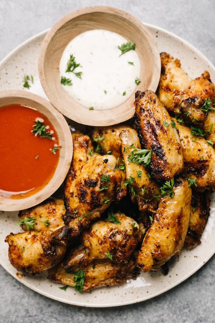 A plate of grilled chicken wings with 2 dipping sauces in small bowls on the side. 