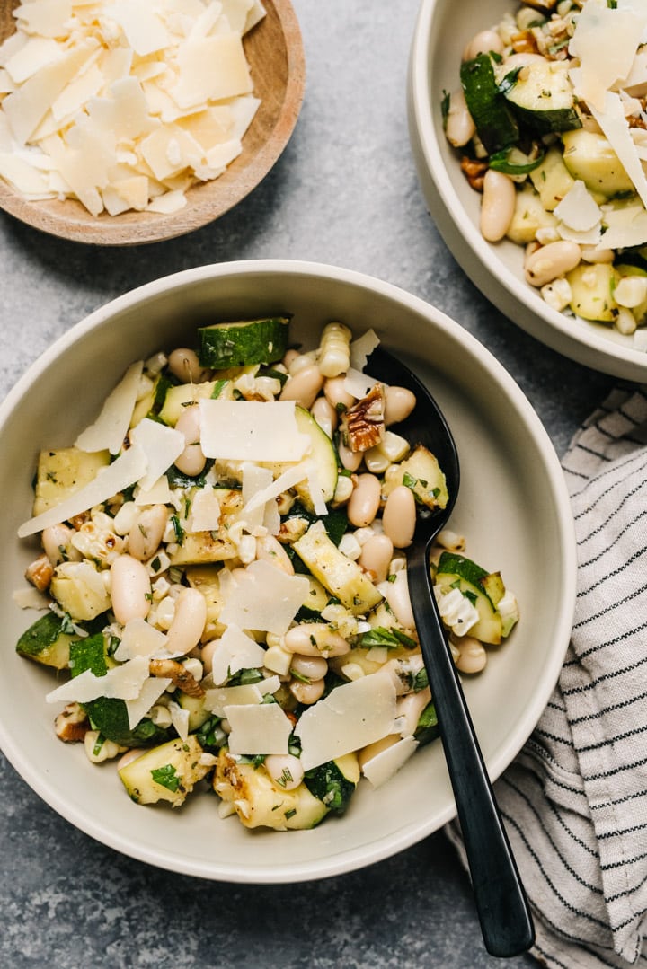 A bowl of zucchini salad with a side bowl of cheese to top.