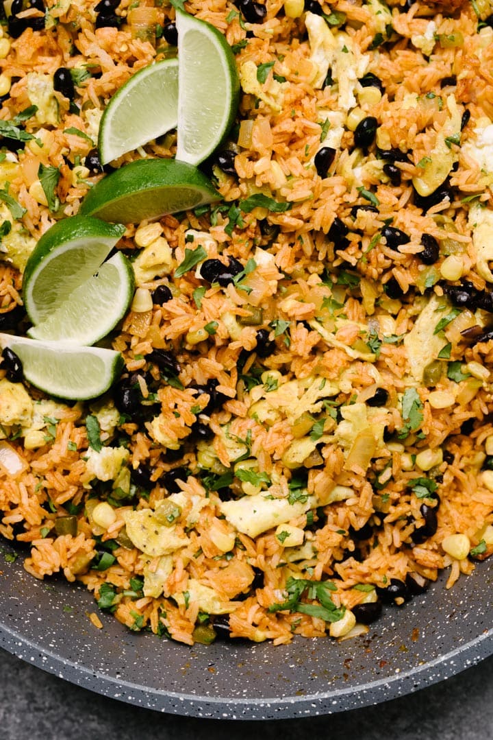 Mexican fried rice in a skillet, garnished with lime wedges and fresh cilantro.