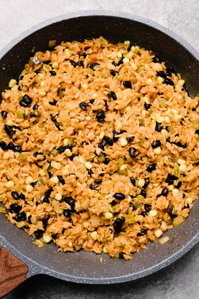 Corn and black beans folded into mexican style fried rice in a skillet.
