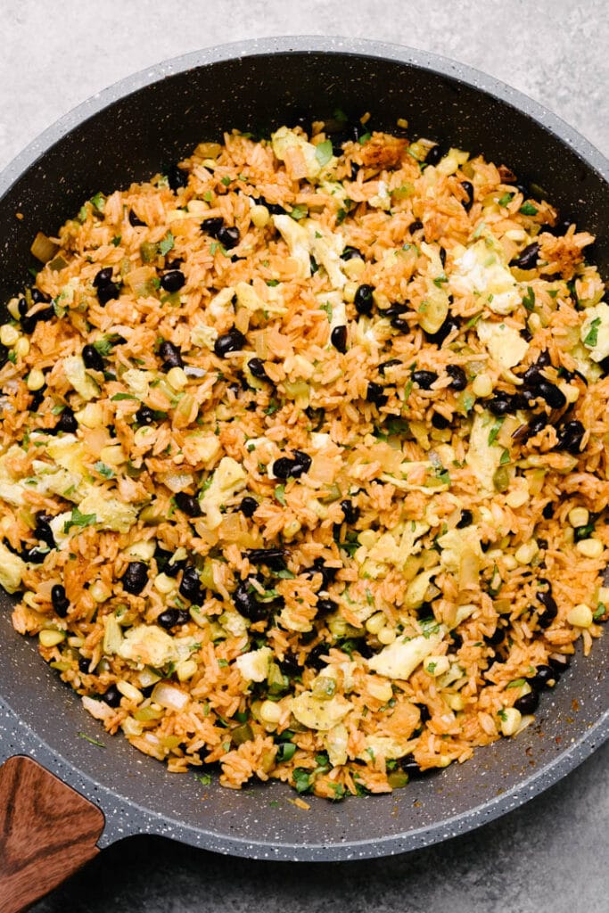 Mexican fried rice in a large skillet with black beans, corn, eggs, and seasonings.