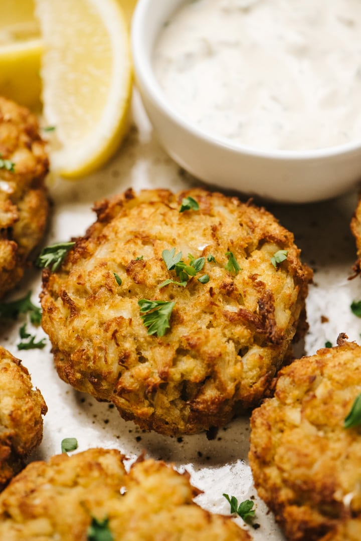 Close up of several crab cakes and a bowl of tartar sauce. 