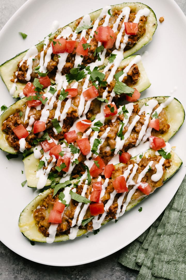 Chicken taco stuffed zucchini boats on a plate with sour cream and salsa. 