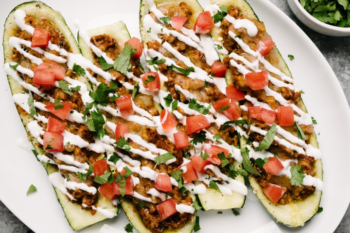 Chicken taco zucchini boats with salsa and sour cream on a plate. 