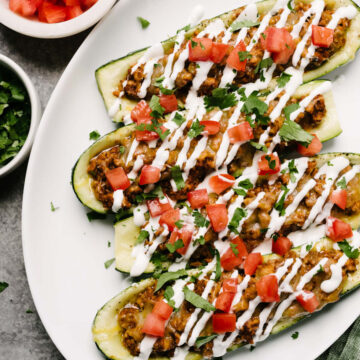 A white plate with chicken taco zucchini boats topped with sour cream and salsa.