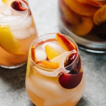 A pitcher and 2 wine glasses filled with peach sangria.