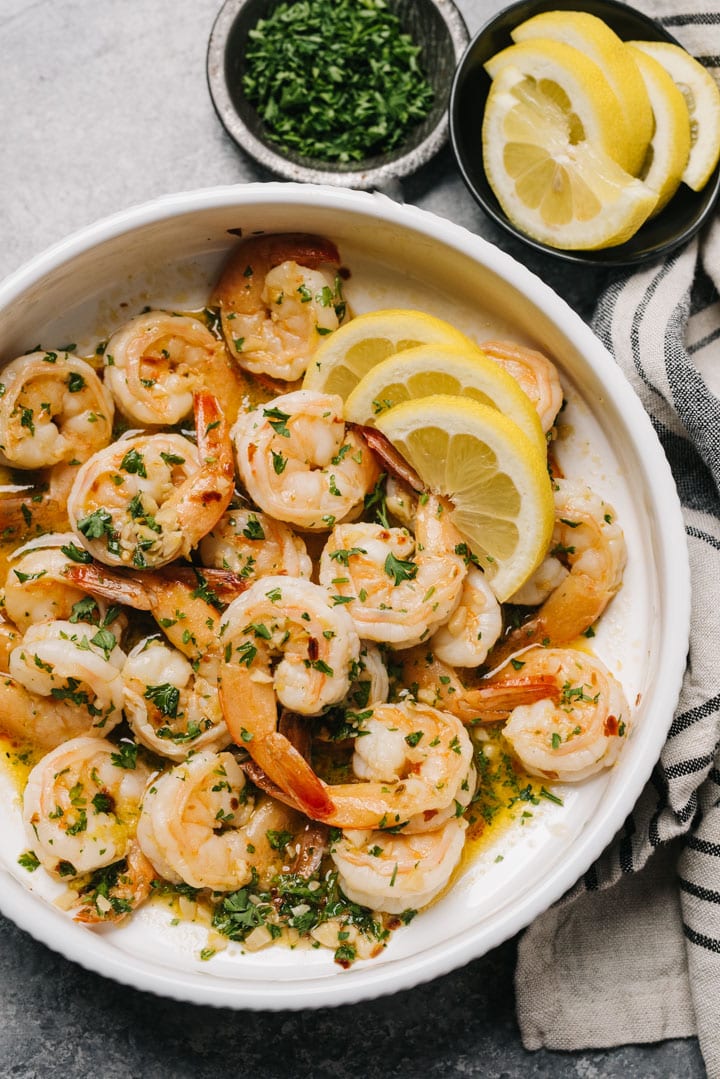 A bowl of lemony garlic butter shrimp with lemons, fresh parsley, and a linen napkin on the side.
