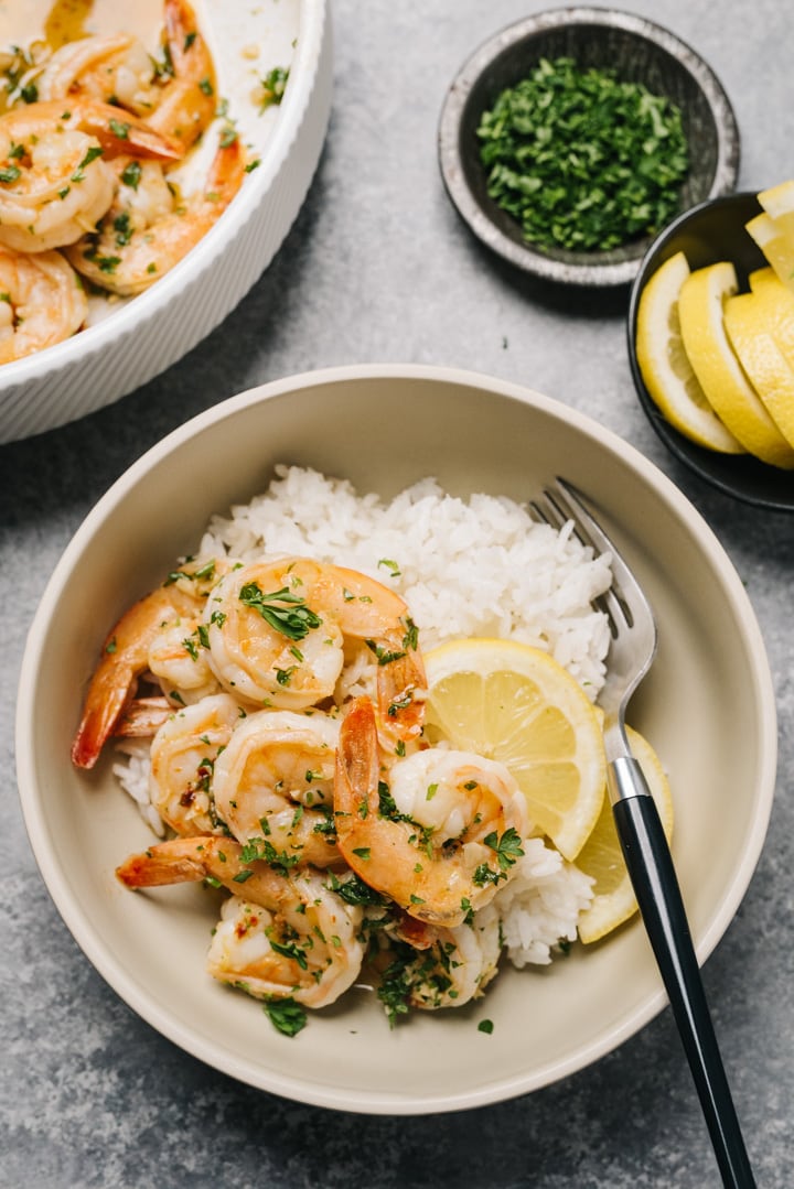 A bowl of shrimp served over white rice, with a side of lemon wedges. 