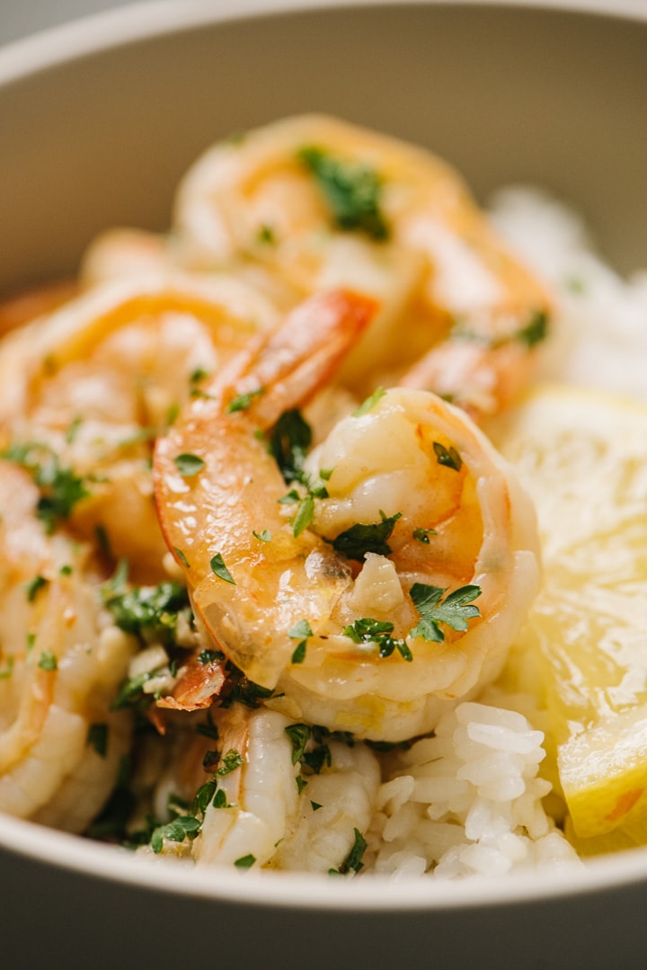 Side view, detail of lemon butter shrimp over rice in a tan bowl with lemon slices to garnish.