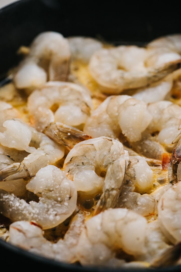 Raw shrimp seasoned with salt in a skillet.