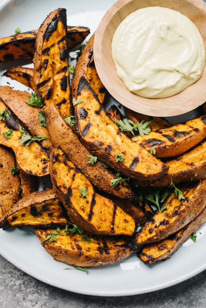 Grilled sweet potato wedges on a plate with avocado aioli on the side. 