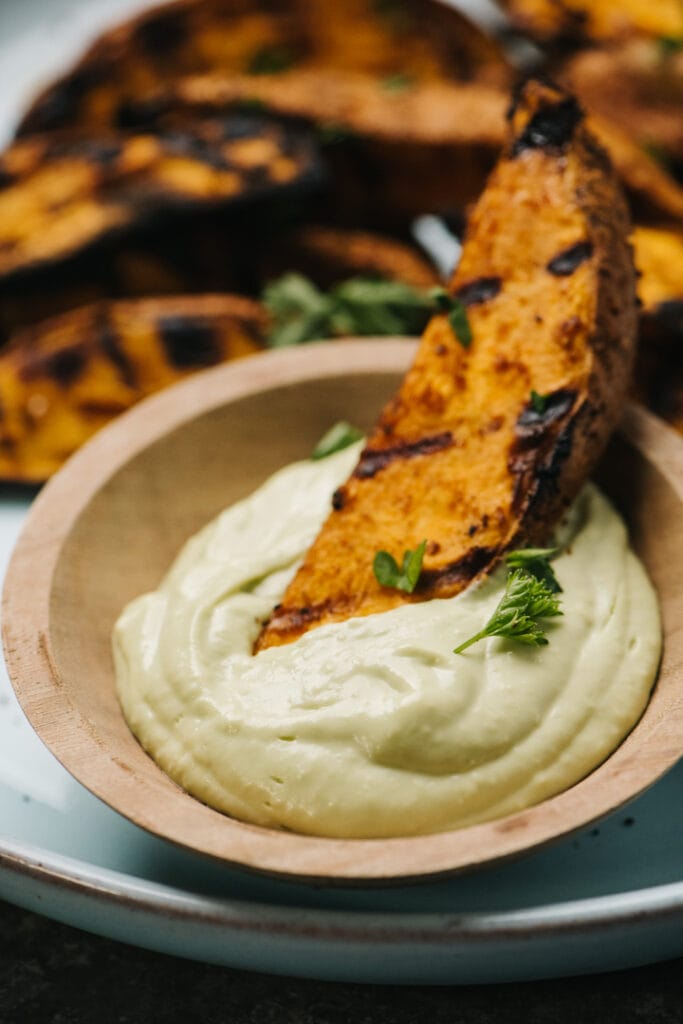 A sweet potato wedge being dipped in avocado aioli dipping sauce. 