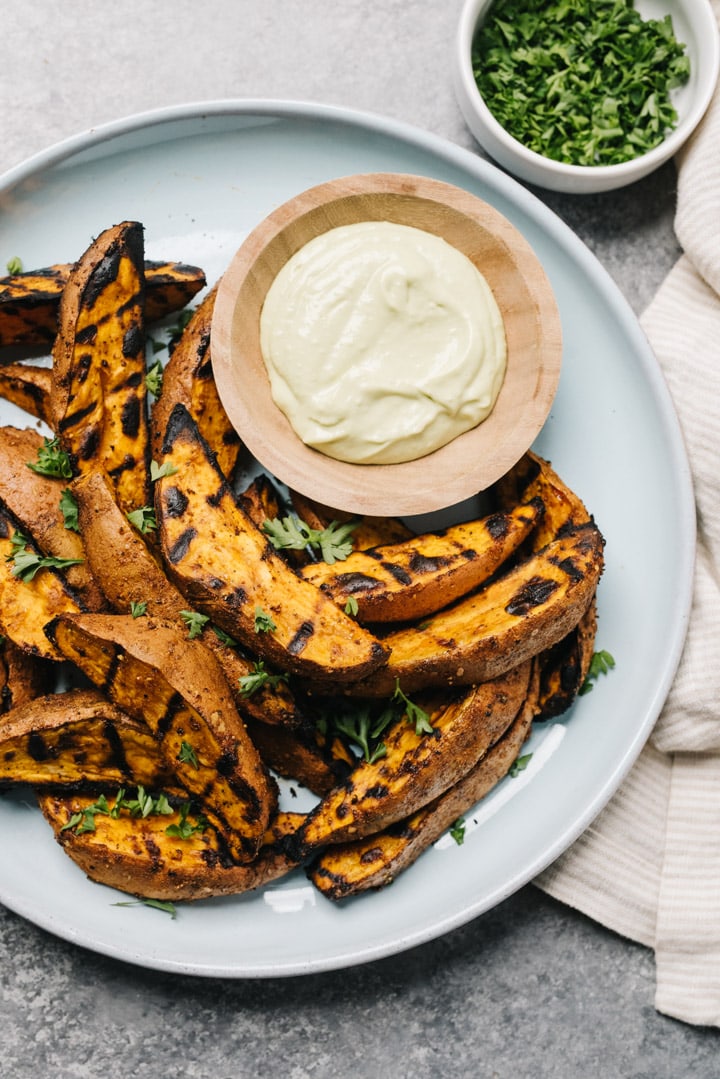Grilled sweet potatoes on a plate with aioli sauce on the side. 