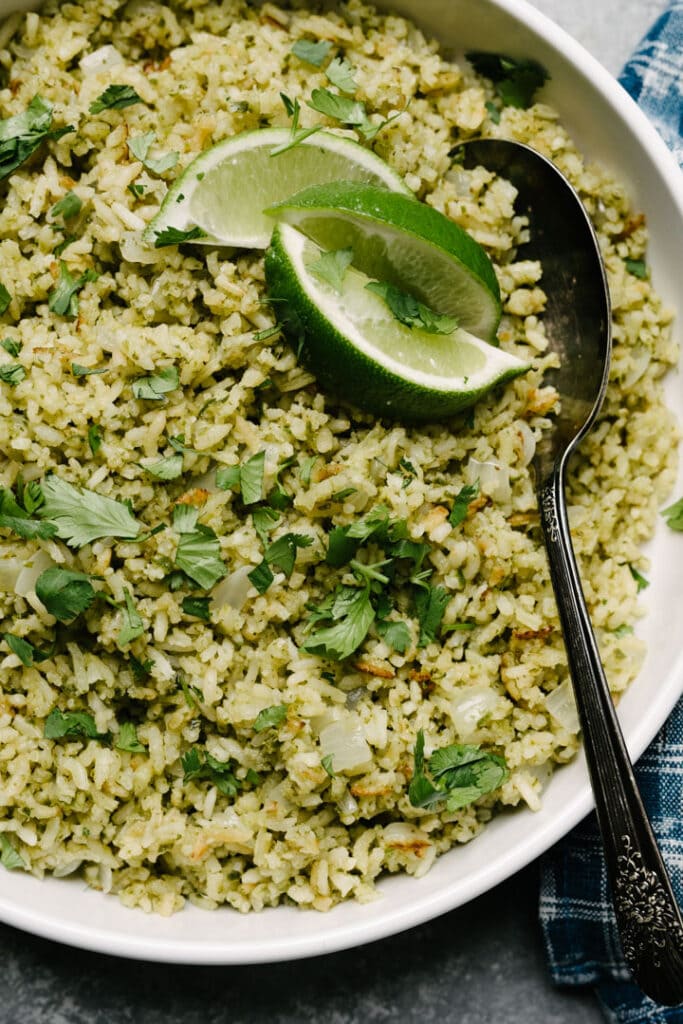 Close up photo of green rice in a bowl with lime and a spoon.