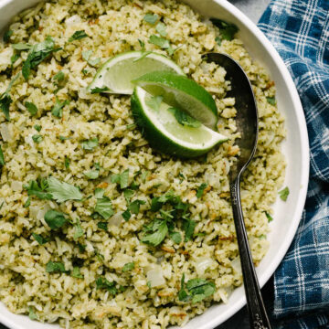 A square picture of Mexican green rice in a bowl with a lime wedge.