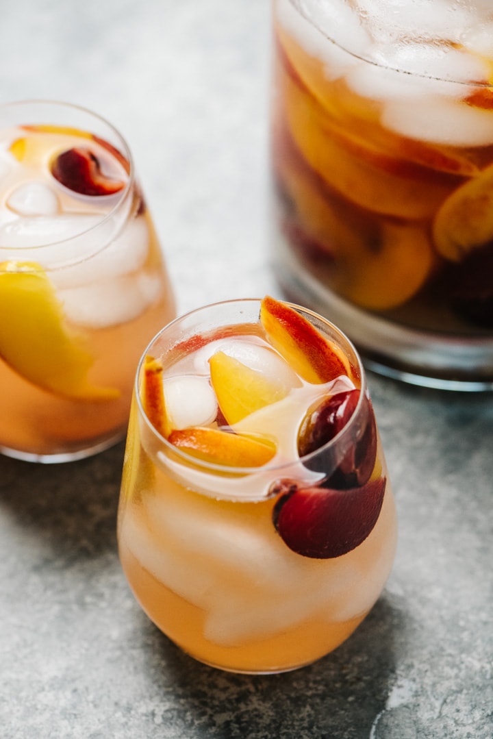 Two stemless wine glasses filled with peach sangria, with a pitcher in the background.
