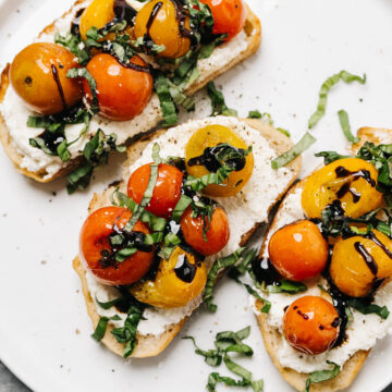 Three slices of ricotta toast topped with tomatoes, basil, and balsamic glaze on a white plate.