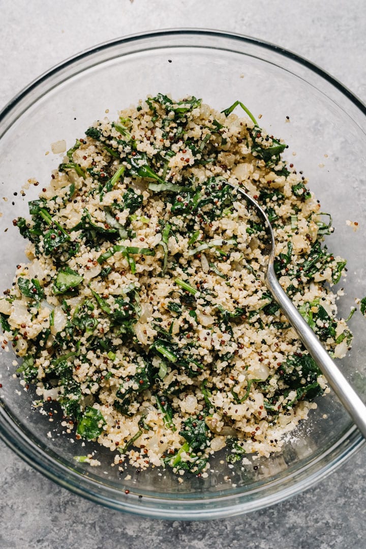 Cooked quinoa mixed with spinach, onions, bread crumbs, and parmesan cheese in a glass mixing bowl.
