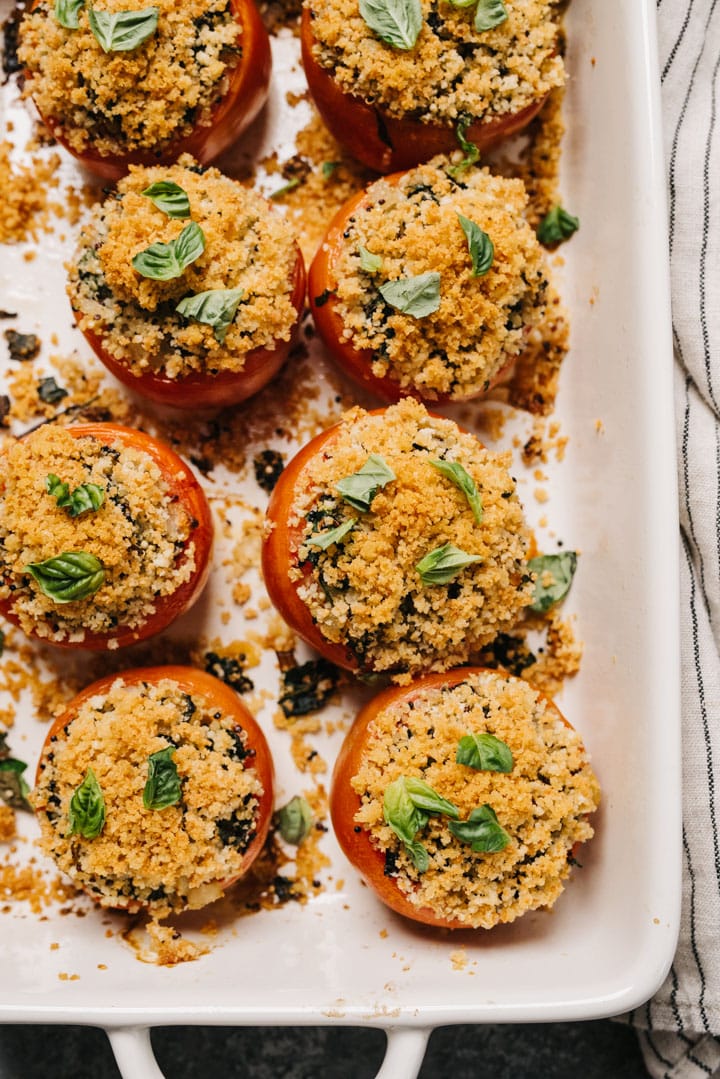 Healthy stuffed tomatoes with quinoa, basil, and parmesan cheese in a baking dish, with a striped linen napkin to the side.