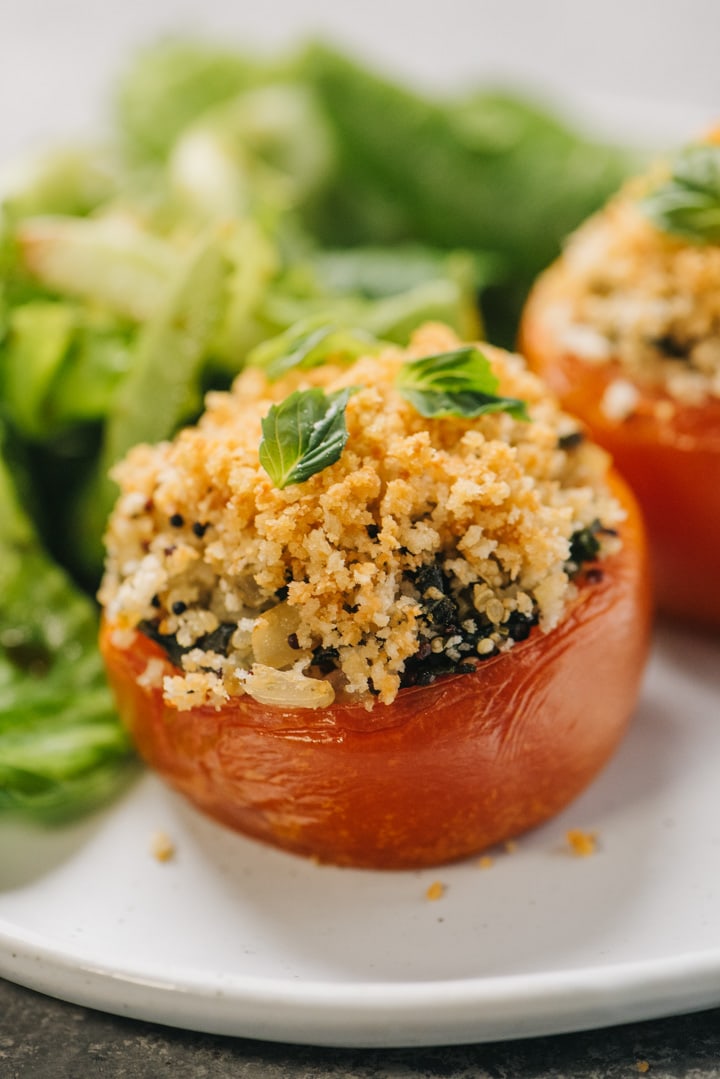 Two vegetarian stuffed tomatoes on a white plate with a green salad.