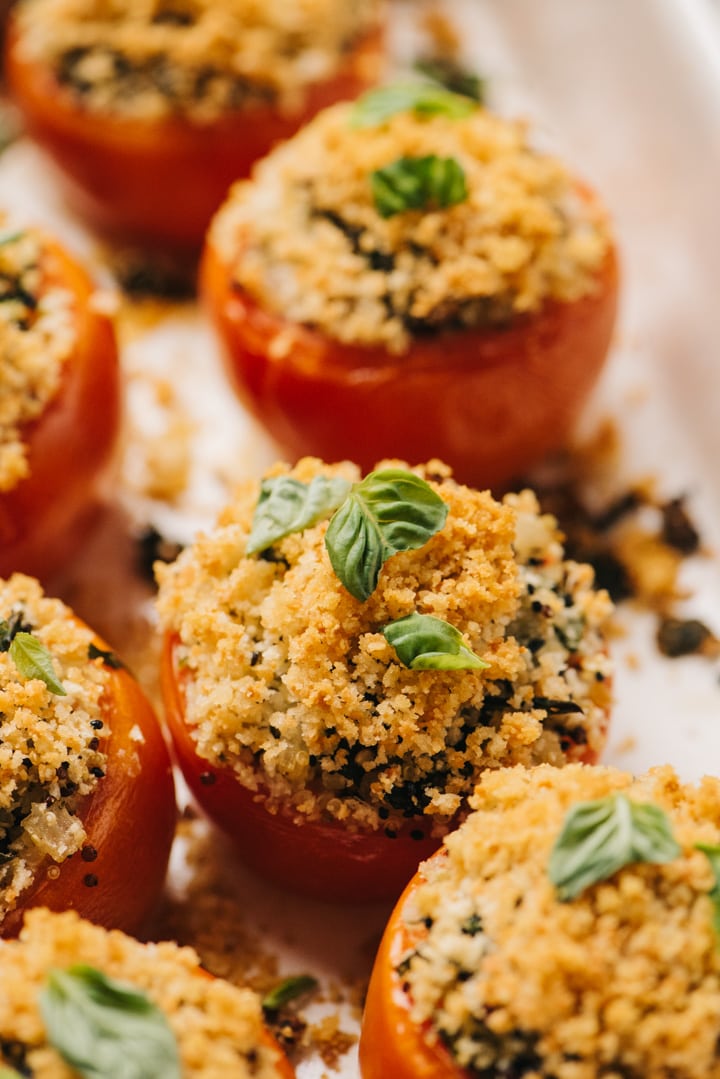 Side view, quinoa stuffed tomatoes garnished with fresh basil in a casserole dish.