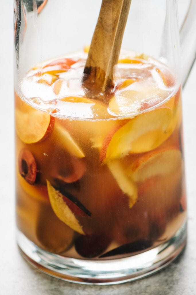 A glass pitcher with a wooden spoon stirring sangria. 