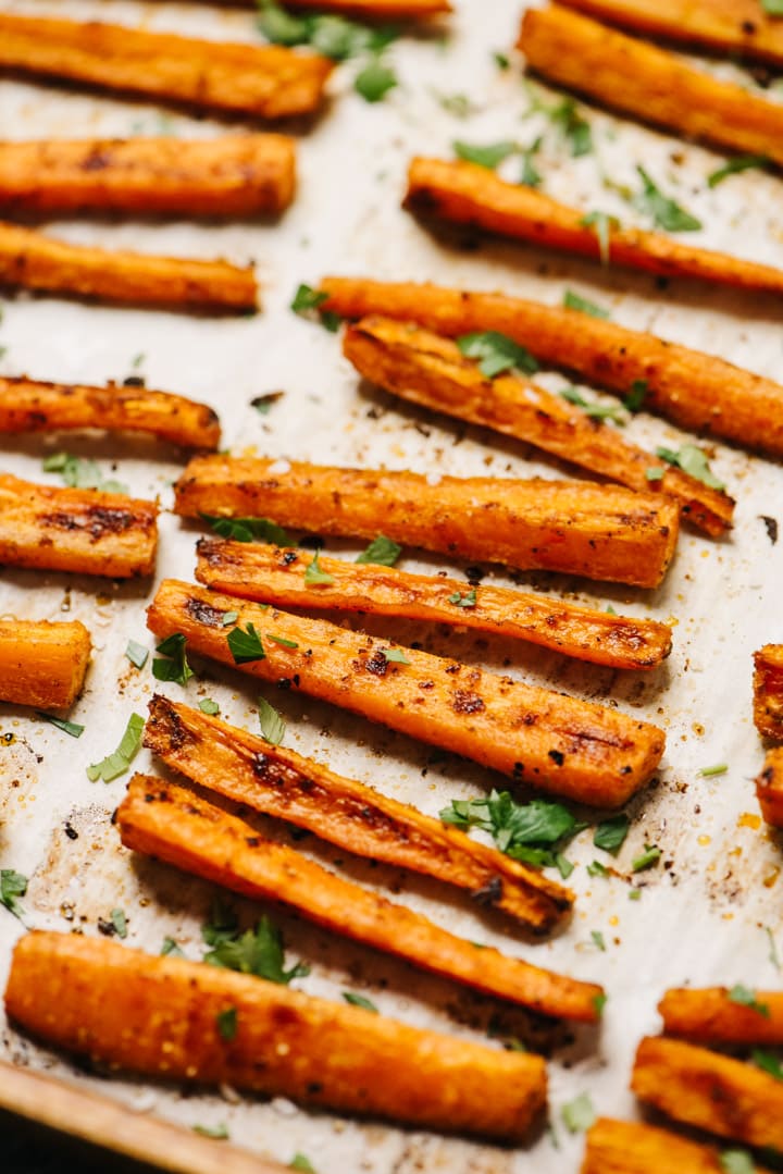 Side view, oven baked carrot fries on a sheet pan, garnished with chopped basil and flaky sea salt.