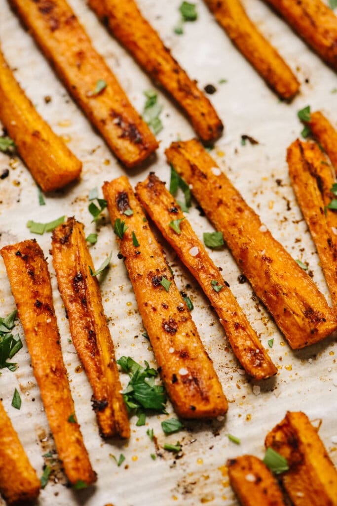 Side view, roasted carrot fries on a parchment lined baking sheet.