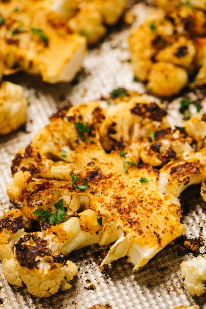 Side view, crispy oven roasted cauliflower steaks on a baking sheet, garnished with fresh parsley.