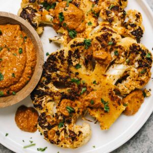 Roasted cauliflower steaks on a plate with sauce on the side.