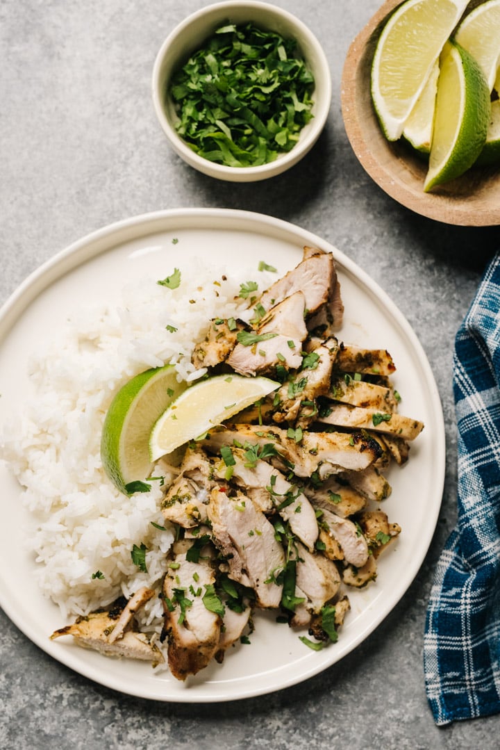 A plate with rice and sliced cilantro lime chicken with lime wedges and cilantro to the side. 