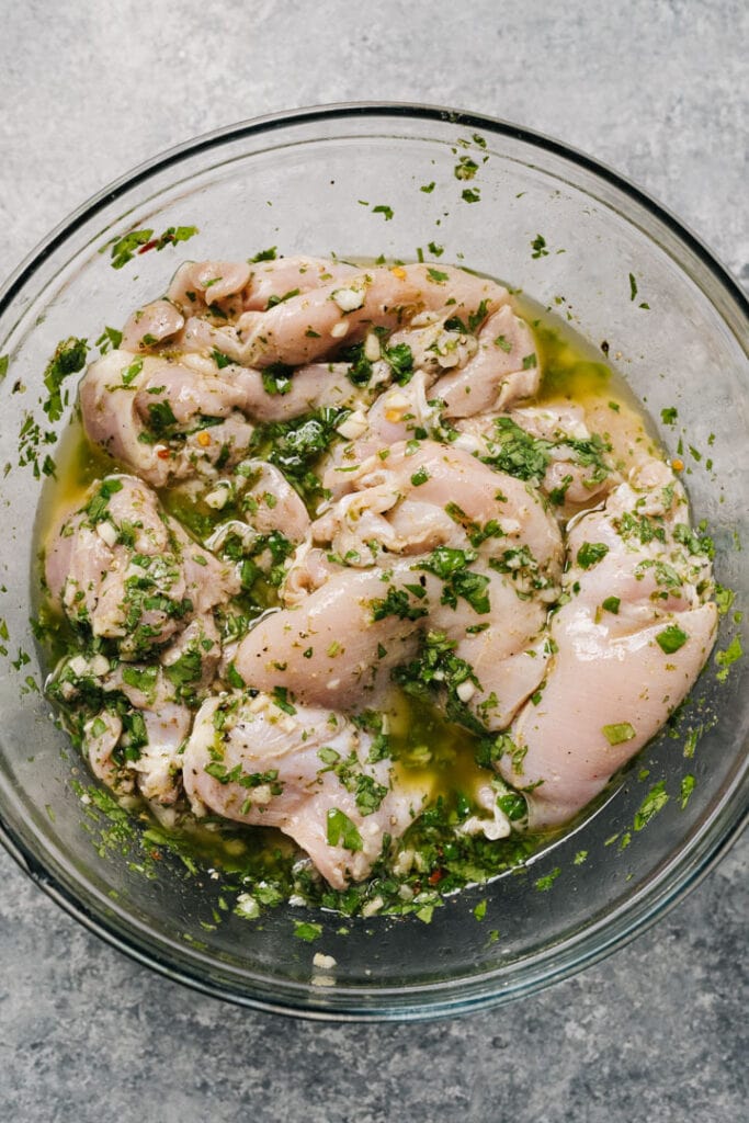 Chicken thighs marinating in a glass mixing bowl.
