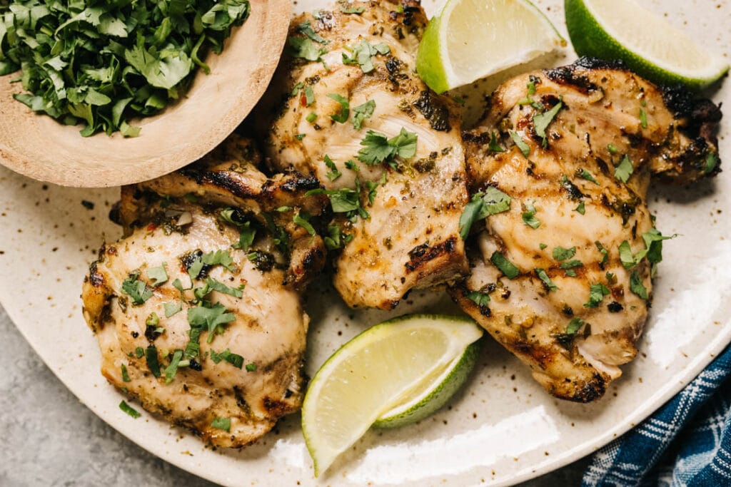 Cilantro lime chicken on a speckled tan plate, garnished with lime wedges and fresh cilantro.